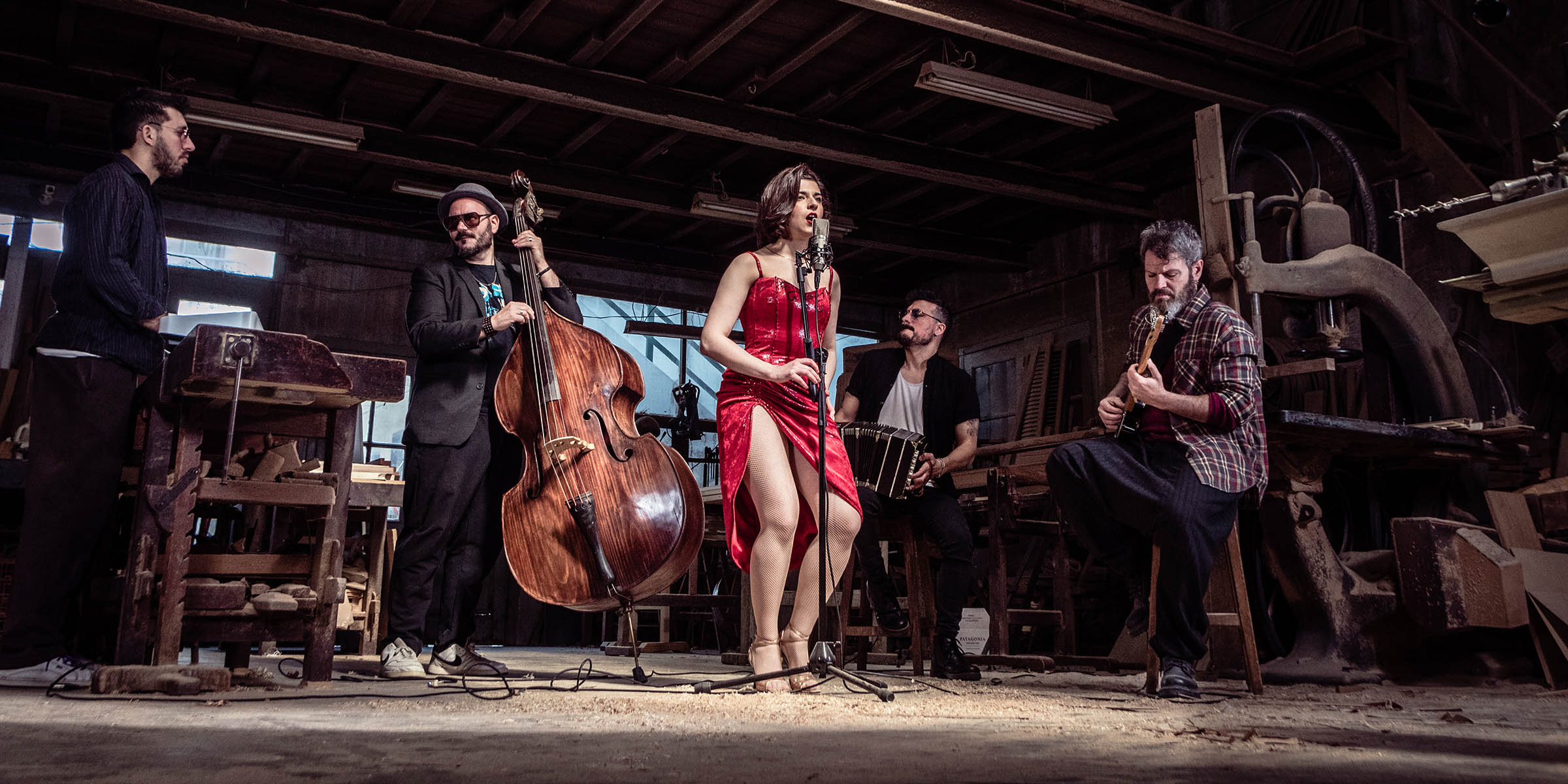 Five people in a band. Vocalist in front of the microphone in a bright red dress.