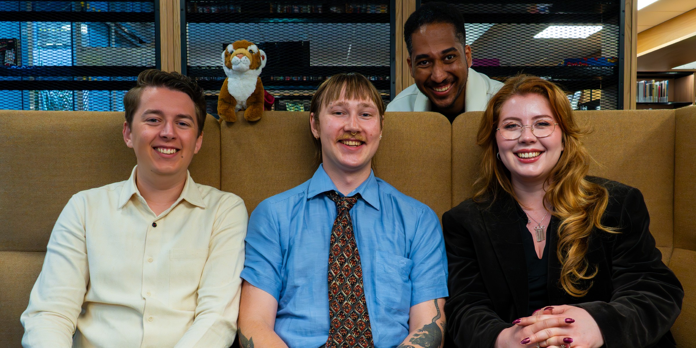 Three people are sitting on a sofa and one is standing behind.