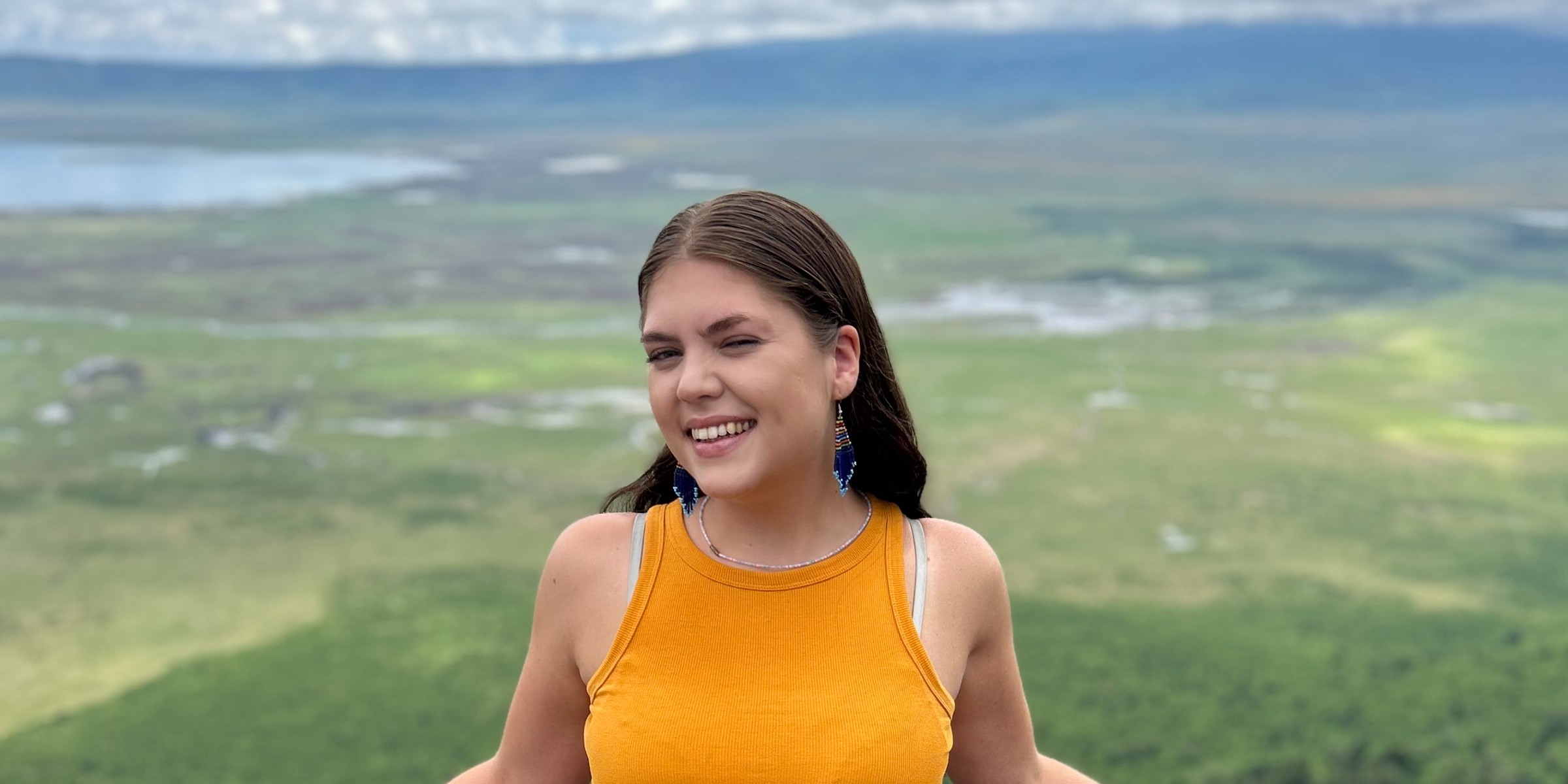 OsloMet-student Eline smiler til kamera med grønt landskap i bakgrunnen.