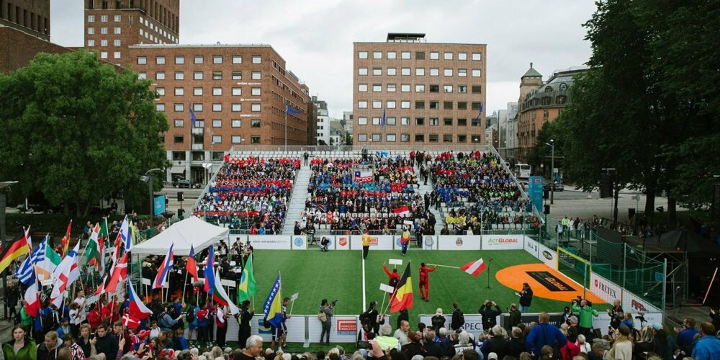 En fotballbane omgitt av mennesker med flagg fra ulike deler av verden og en tribune full av publikummere utenfor Rådhuset i Oslo.